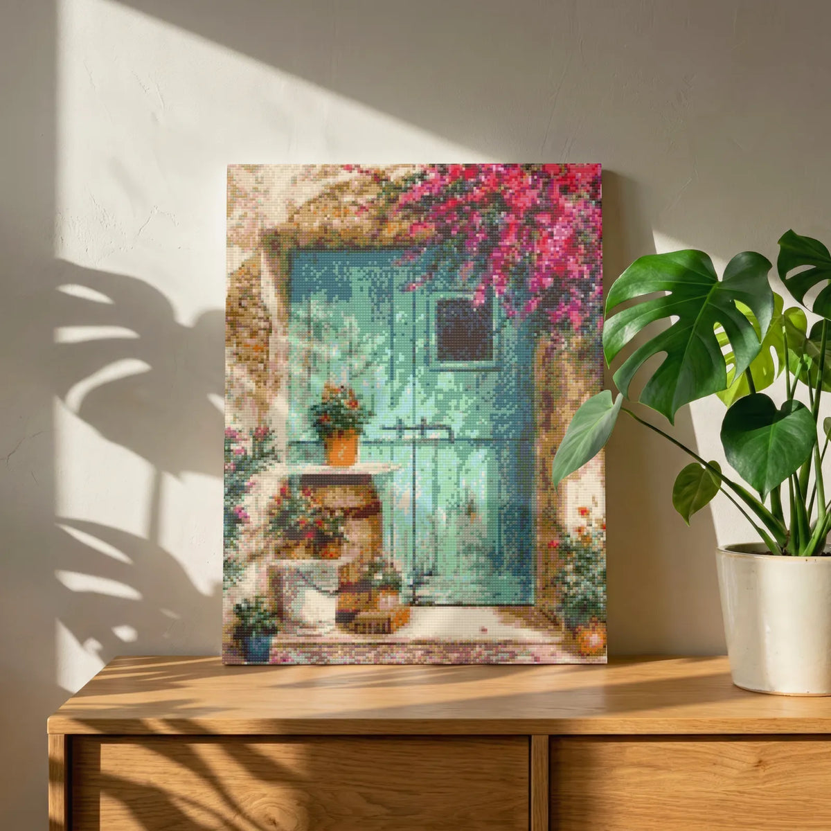 Mediterranean door diamond painting kit, turquoise door and bougainvillea on a wooden sideboard beside a monstera